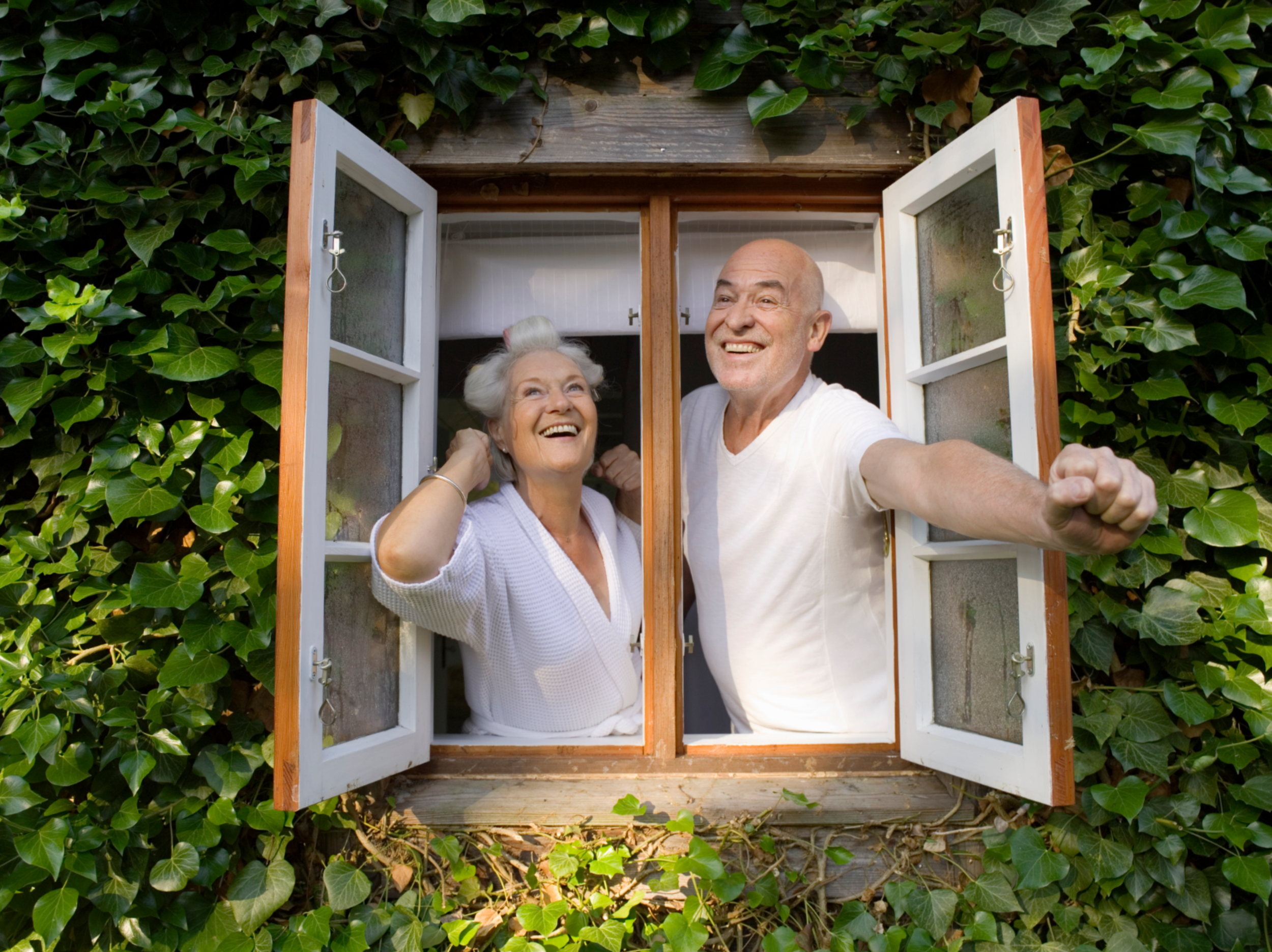 Senior couple opening window in morning, smiling