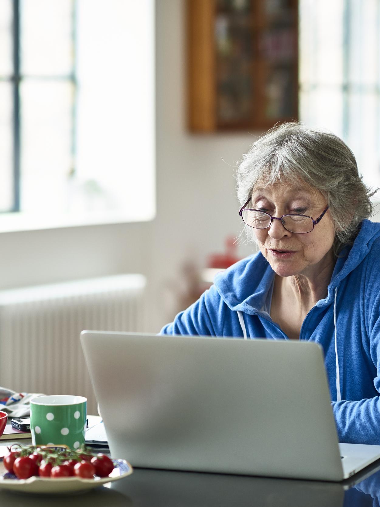 Senior woman wearing glasses using laptop at home