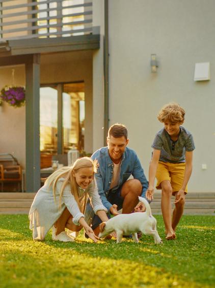 Gezin speelt met een kleine hond in de tuin van hun huis