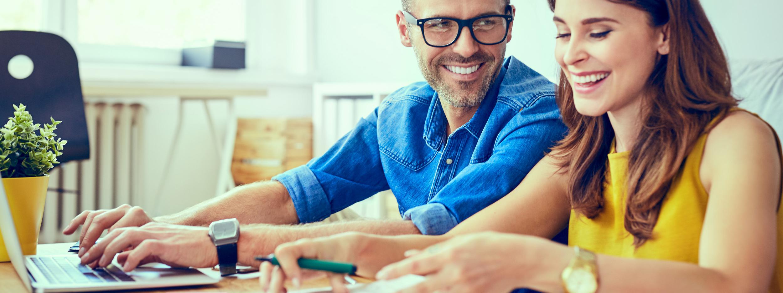 Happy couple at home paying bills with laptop