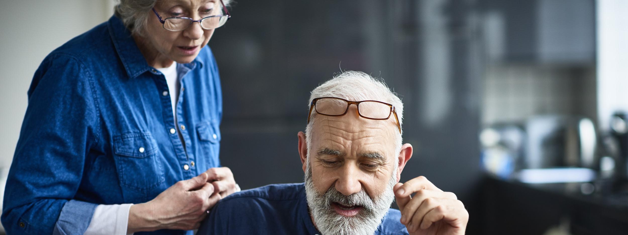 Hipster senior man with beard using laptop and woman watching